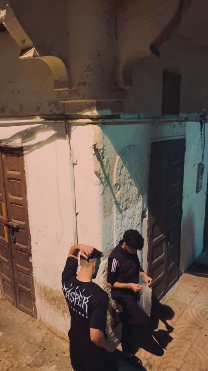 Two friends in printed tees on a whitewashed lane in the village at dusk